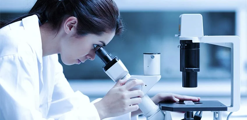 Pesquisadora da UERJ observando uma lâmina ao microscópio em laboratório